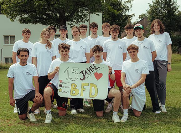 Die Freiwilligen stehen in weißen T-Shirts zum Gruppenfoto zusammen. Bei halten ein Schild mit "15 jahre BFD"